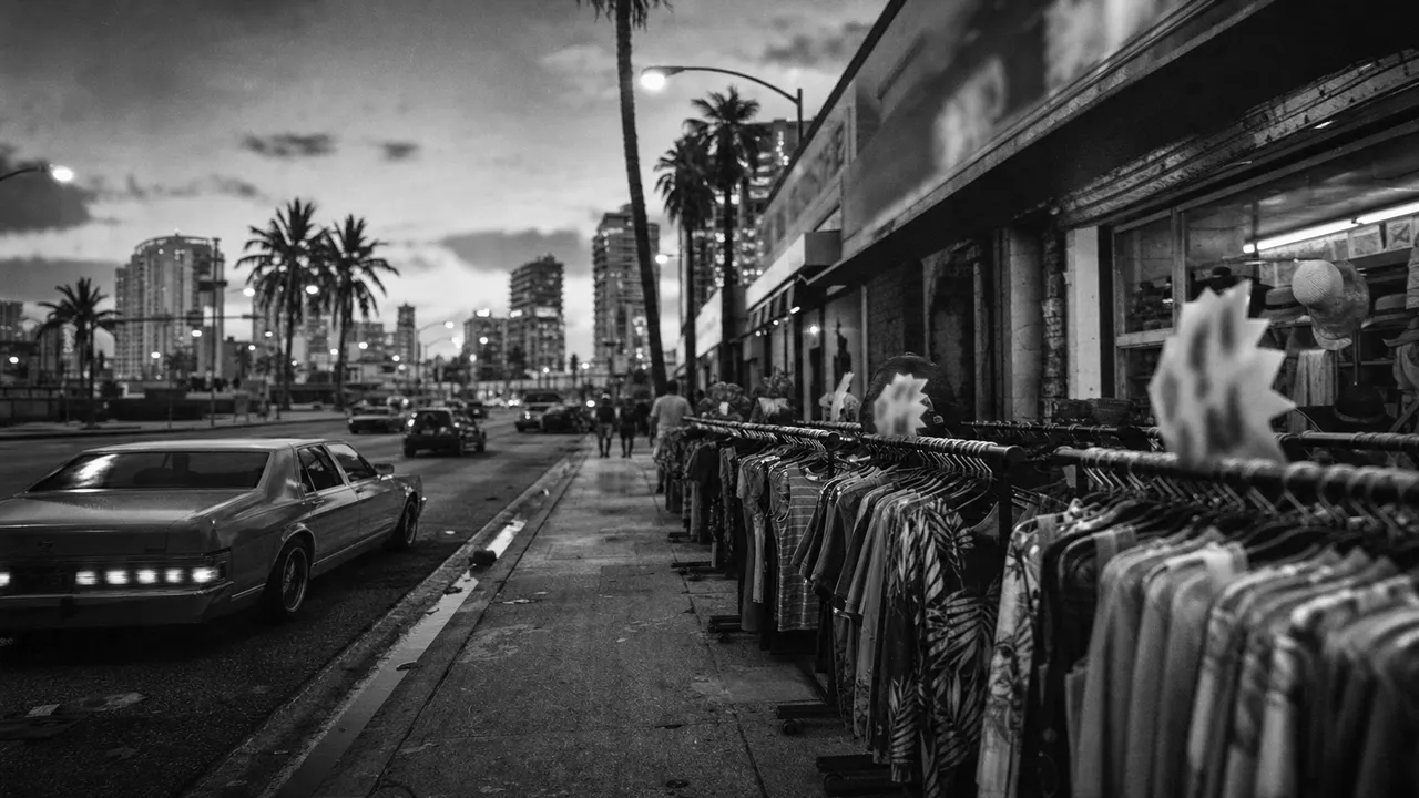 Black and white cinematic view of a discount clothing store with packed racks rolled onto the pavement