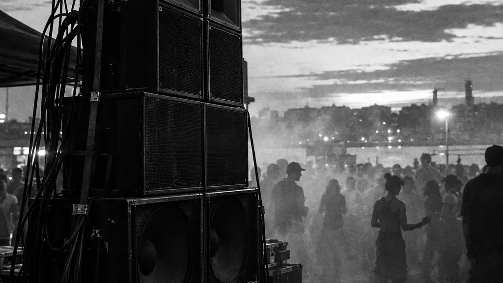 Black and white cinematic photograph of a towering stack of speaker cabinets wired for a street dance