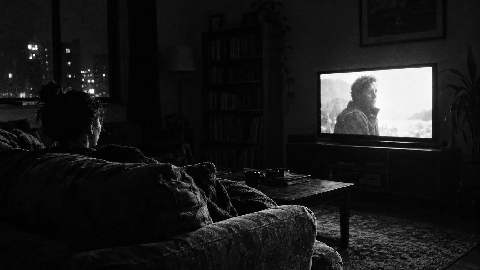 Black and white cinematic shot of a flat screen television glowing in a dark living room