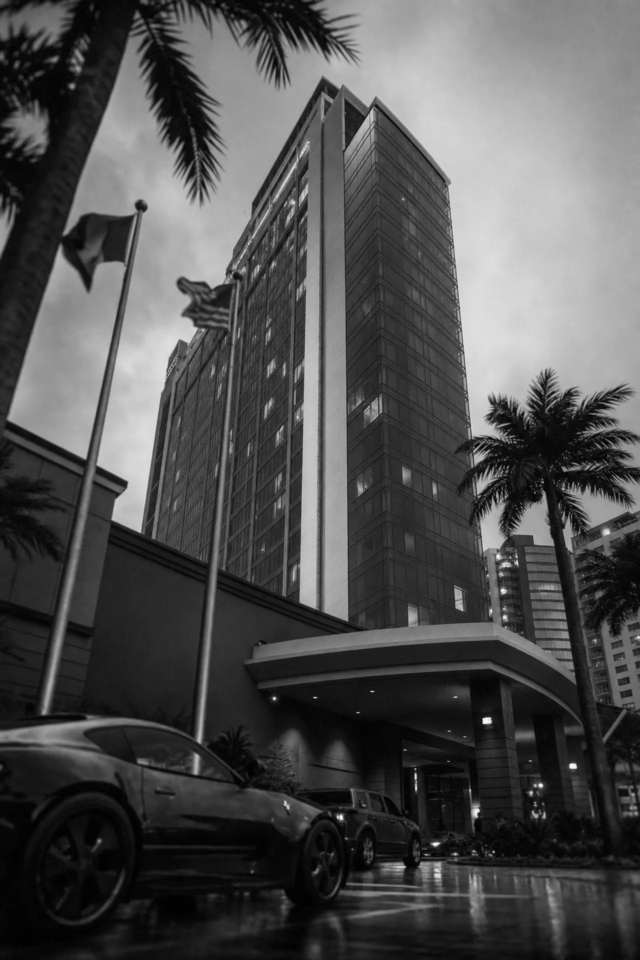 Black and white cinematic upward view of a tall chain hotel tower with a valet canopy at street level