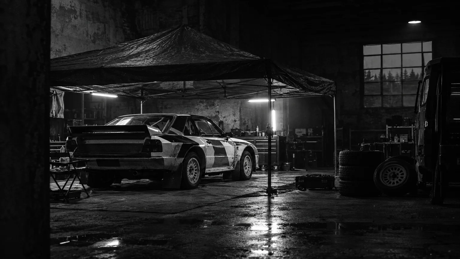 Black and white cinematic photograph of a parked rally car under a tarpaulin in a dim workshop