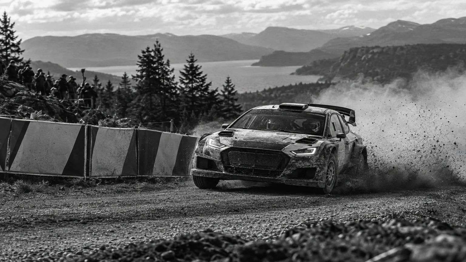 Black and white cinematic photograph of a rally car cornering past sponsor hoardings on a dirt stage