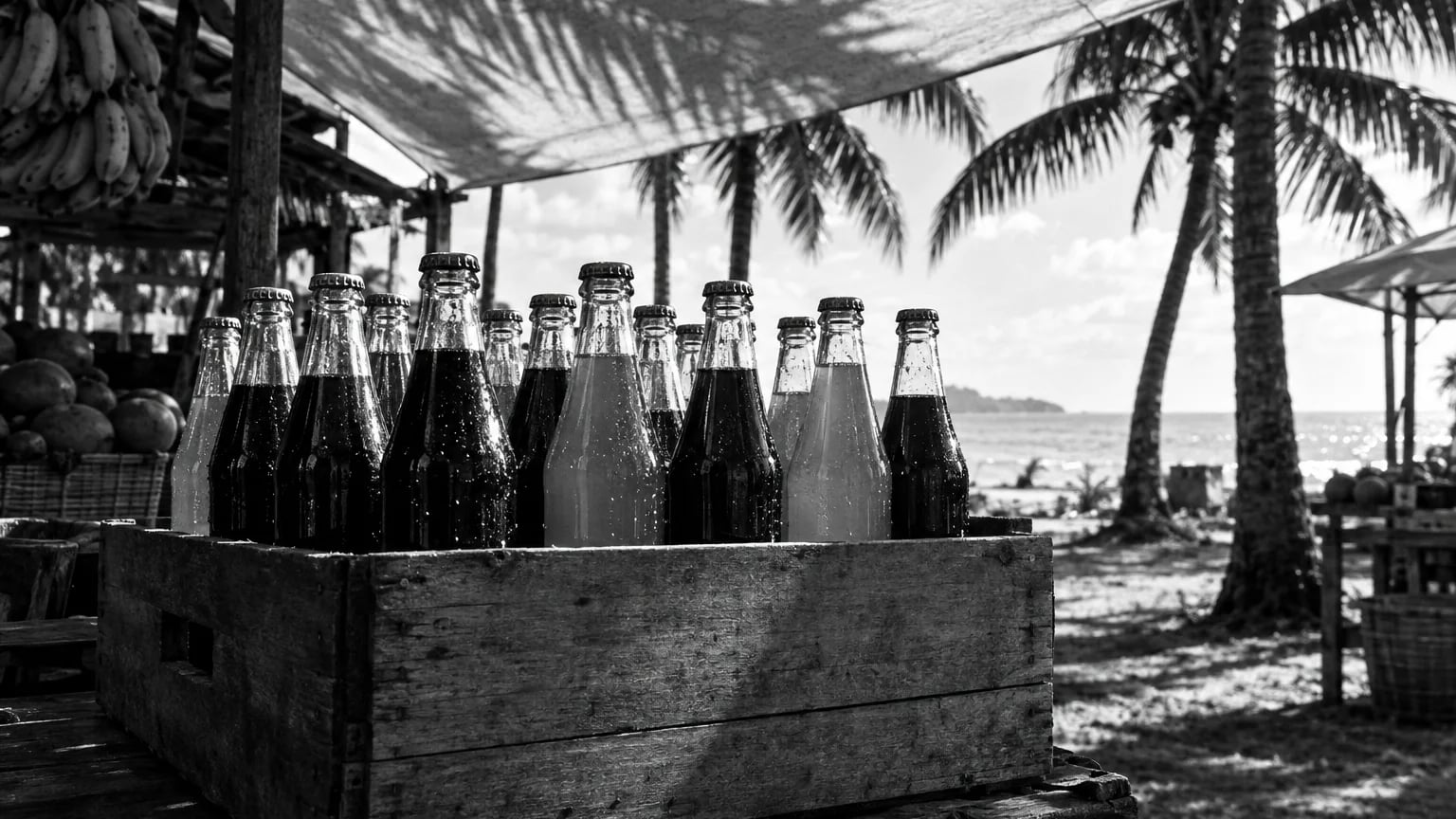 Black and white cinematic photograph of glass soda bottles in a wooden crate on a market stand in tropical light