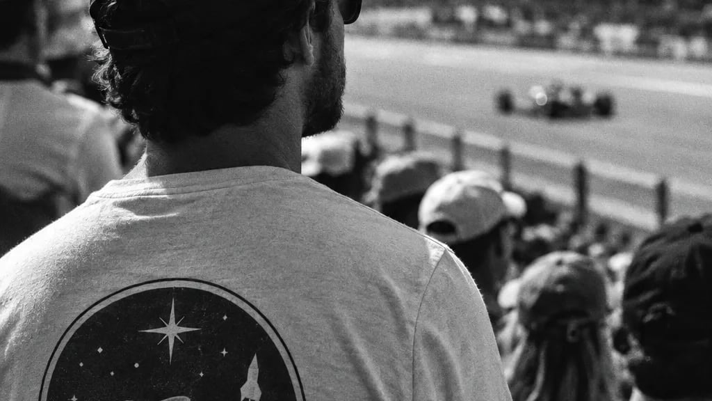 Black and white cinematic detail of a t-shirt with a round space agency styled logo, worn in a crowd