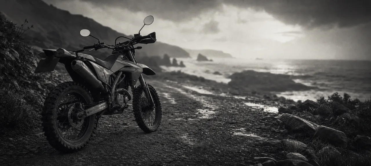 Black and white cinematic concept image of a nimble Japanese dual-sport motorcycle on a gravel coastal trail