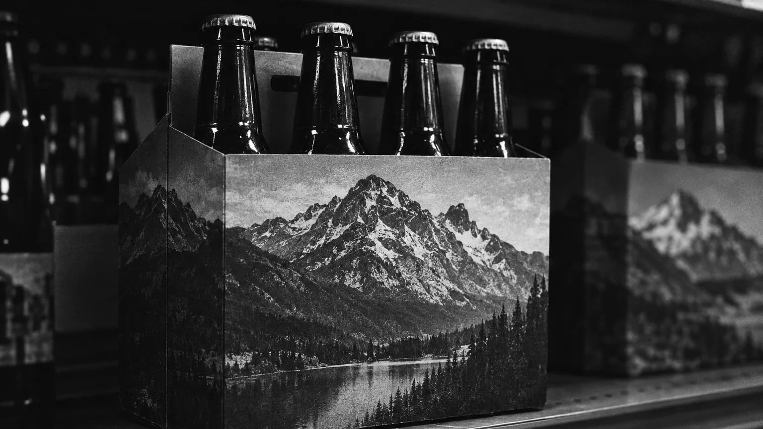 Black and white photo of a beer six pack on a shop shelf, mountain artwork printed across the cardboard carrier