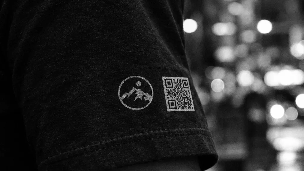 Black and white cinematic detail of a printed t-shirt sleeve showing a round music app logo and scan code