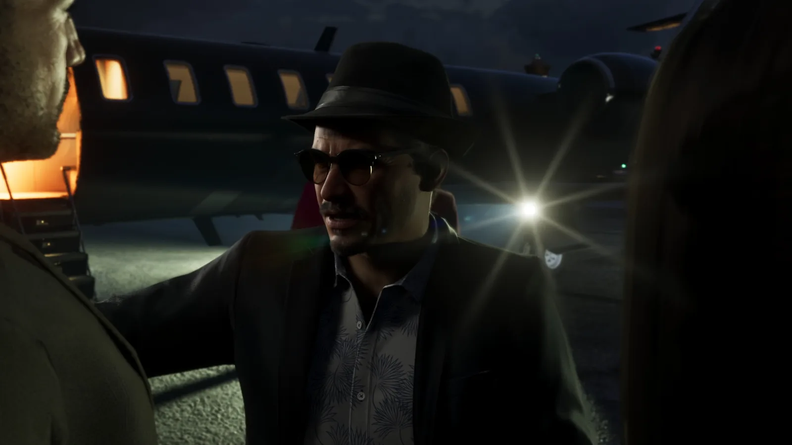 Andres de Leon in a hat and sunglasses beside a car on a night-time airfield in GTA 6.