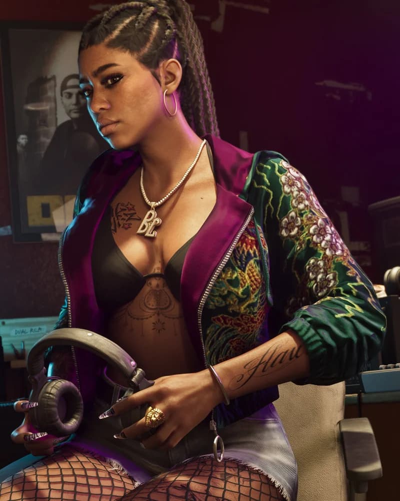 Bae-Luxe in a recording studio, wearing a floral-embroidered jacket over a black top, hoop earrings, with a "BL" diamond pendant.