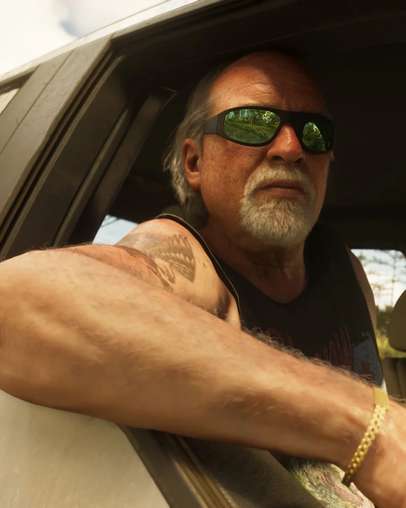 Brian Heder leaning out of a truck window in the Leonida swamps, wearing wraparound sunglasses, a black tank top, and a heavy gold bracelet.