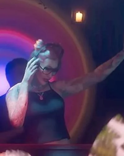 Female DJ behind a club booth, Trailer 2 nightclub sequence.