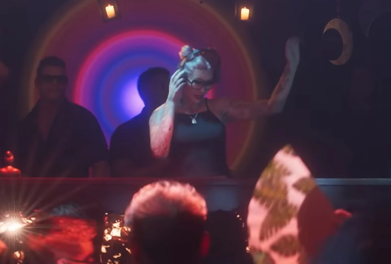 Female DJ behind a club booth, Trailer 2 nightclub sequence.
