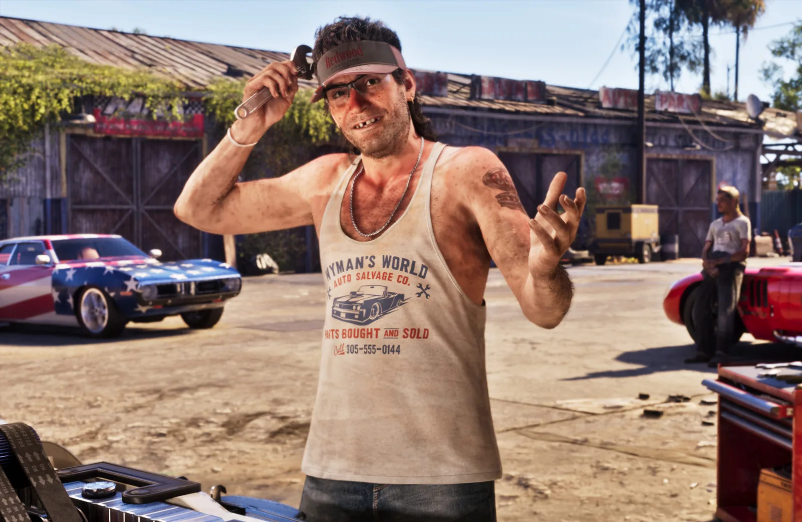 Wyman in his Port Gellhorn salvage yard, wearing a Redwood visor and a grease-stained Wyman's World Auto Salvage Co. tank top while holding a wrench, with classic project cars behind him.