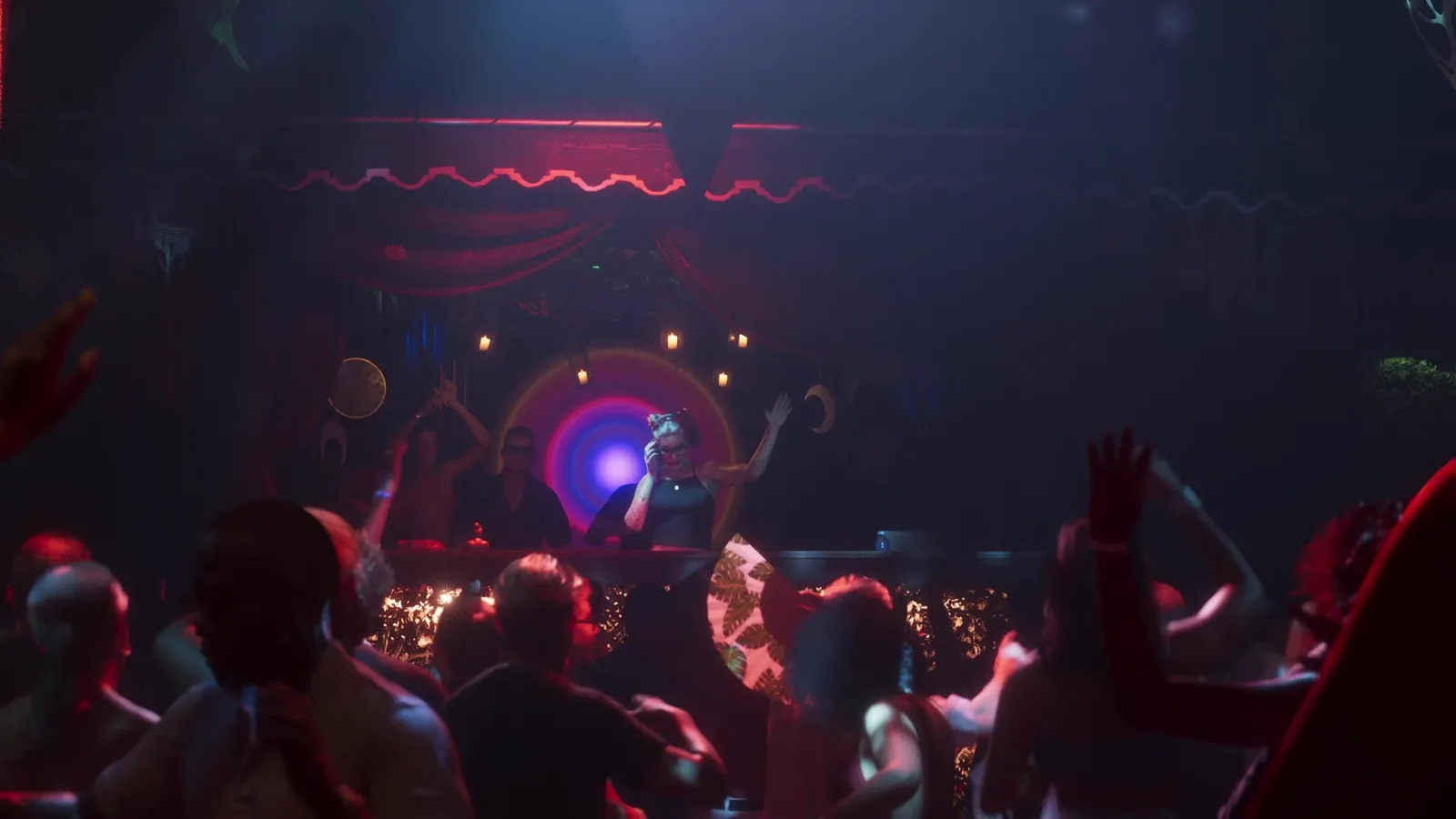A DJ performs behind the decks of a candlelit Vice City club as a crowd dances under red draped ceilings in GTA 6