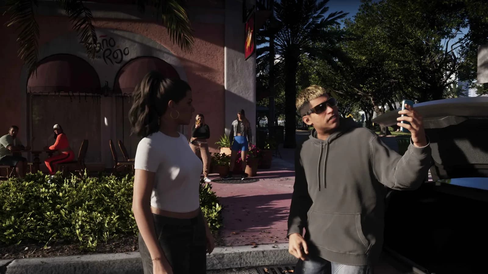 An NPC holds up a phone to film a woman on a sunny Vice City street in GTA 6