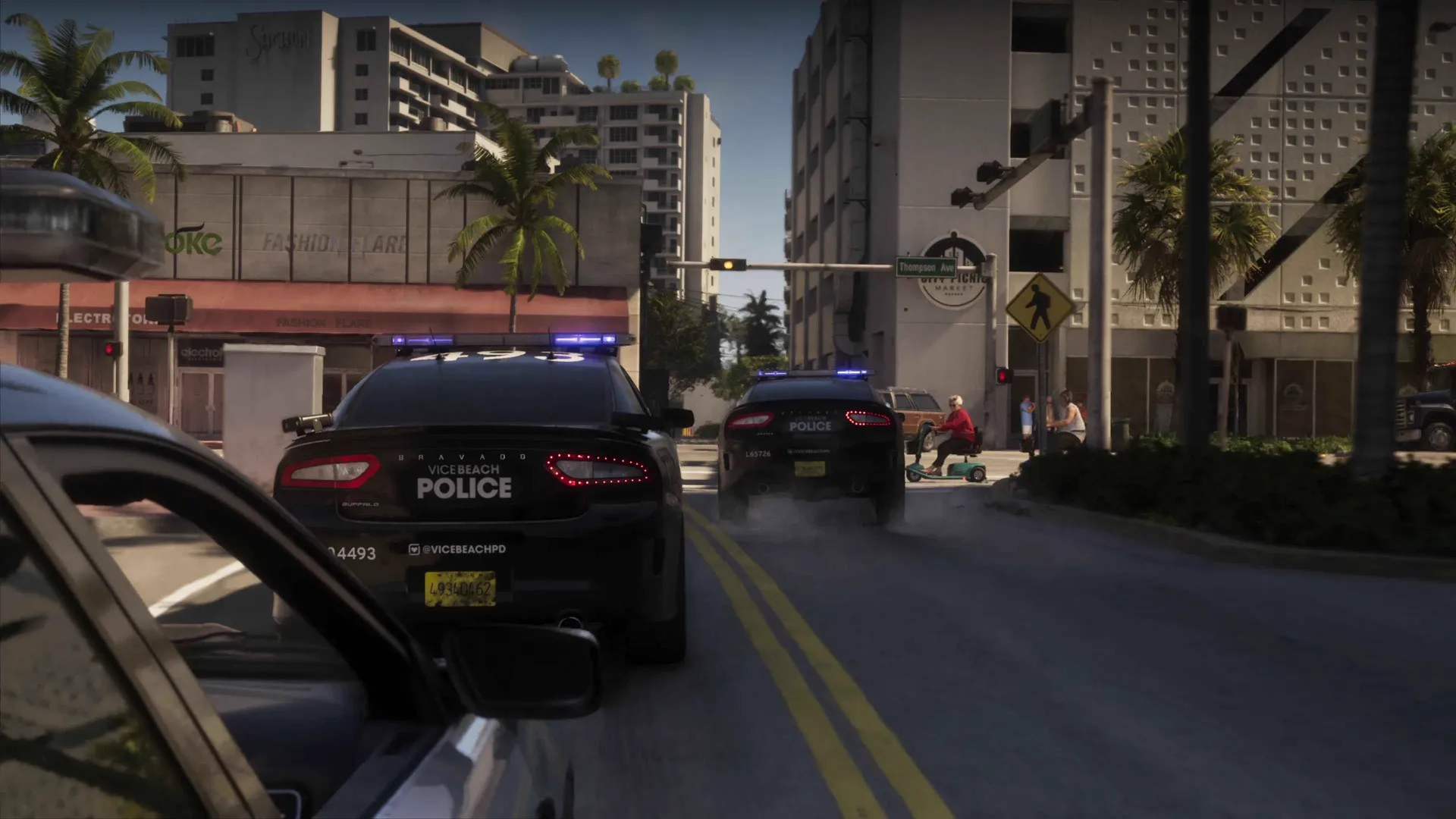 Two Vice Beach Police cruisers with lights flashing box in a car on a palm-lined GTA 6 street while an elderly rider on a mobility scooter waits at the crossing