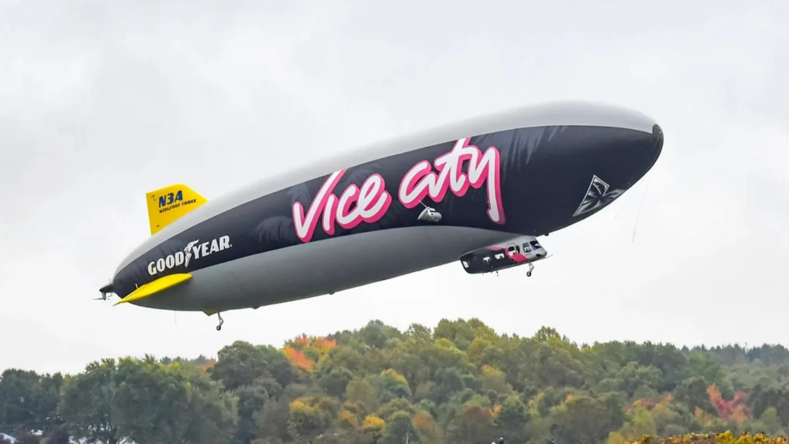 Goodyear’s Wingfoot Three zeppelin in dark Vice City livery with pink lettering flies low over autumn trees, N3A visible on the tail