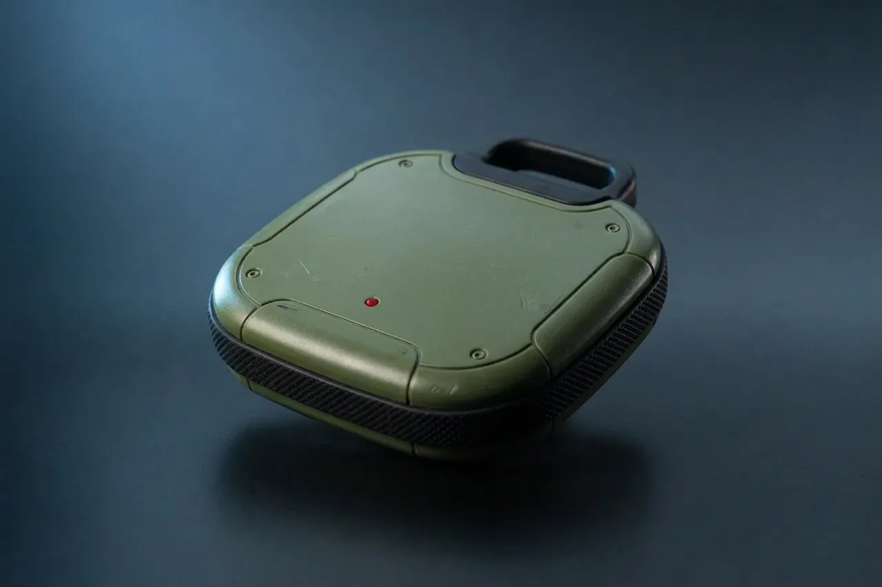 Flat olive-green remote charge with a black finger loop and a red indicator light, placeholder render for the GTA 6 Sticky Bomb