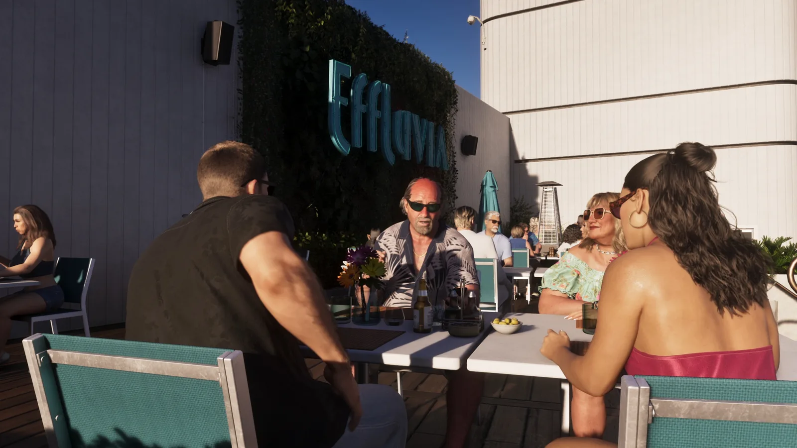 Guests around a table beneath the Effluvia sign in the evening sun