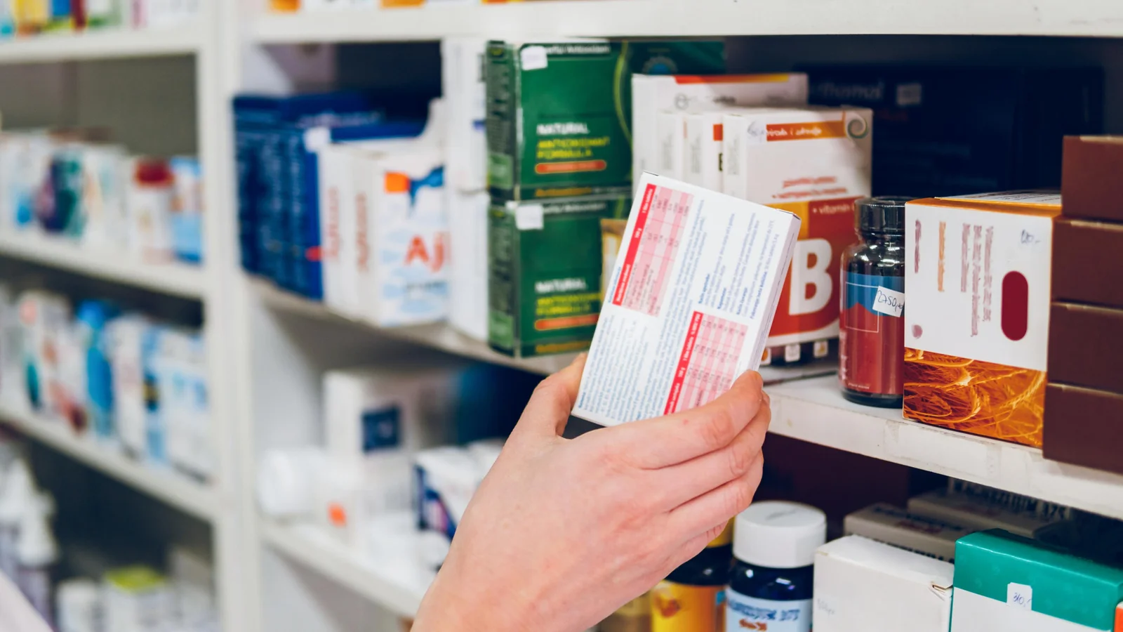 A shopper picking a plain medicine box from a pharmacy shelf