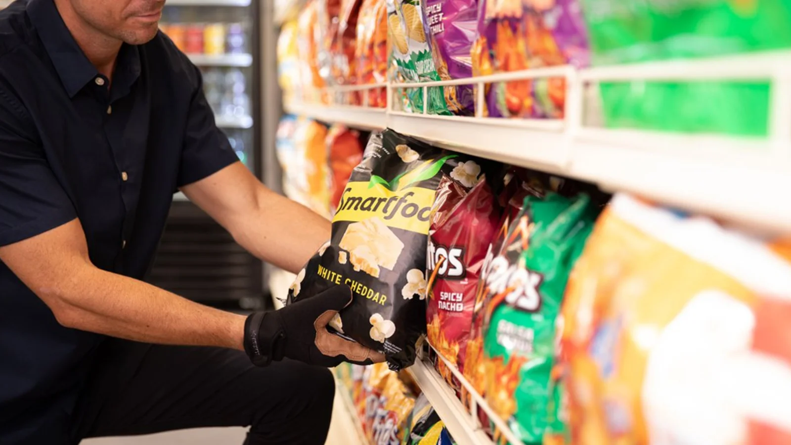 A shopkeeper stocking snack bags on a shop shelf