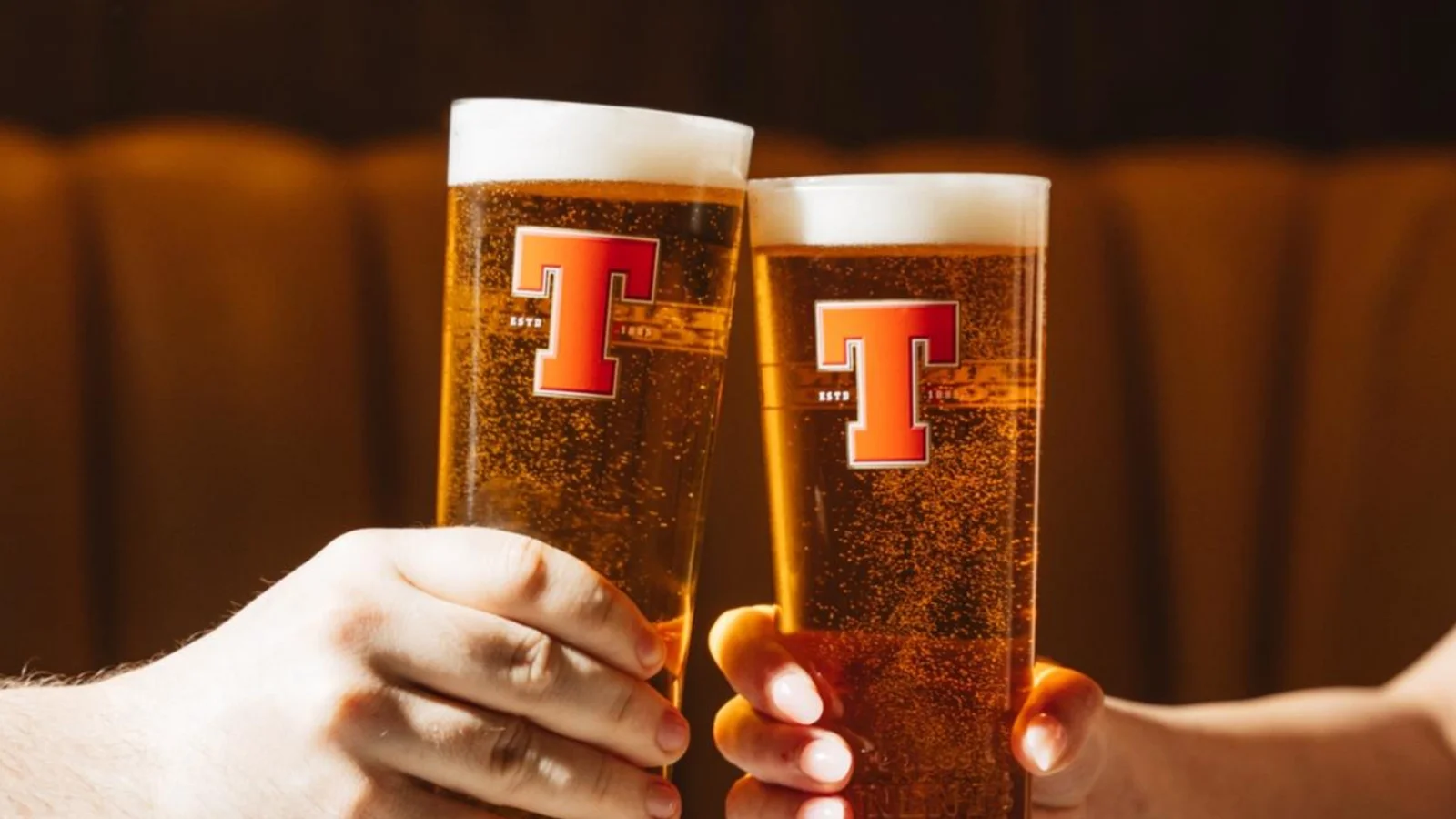 Two pint glasses of Tennent’s lager raised in a toast