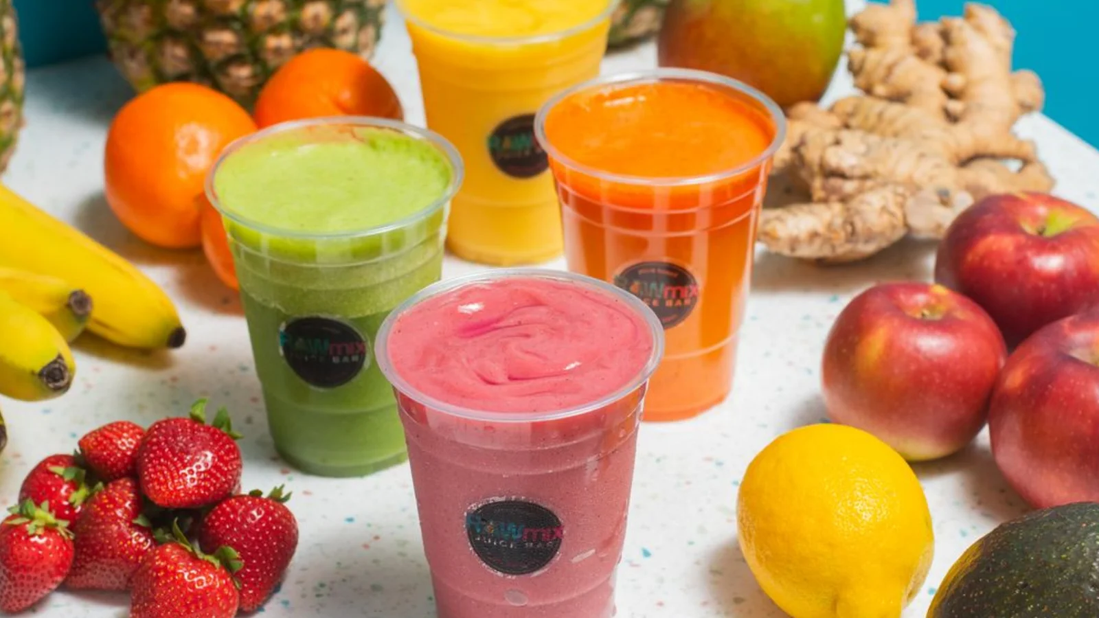 Fresh smoothie cups surrounded by fruit at a juice bar