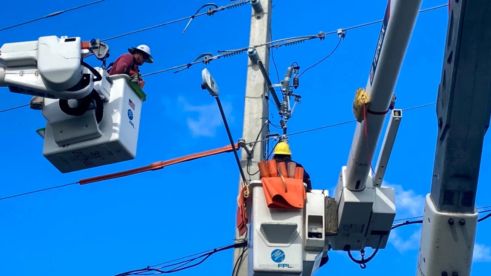 Utility linemen working from bucket trucks on overhead power lines