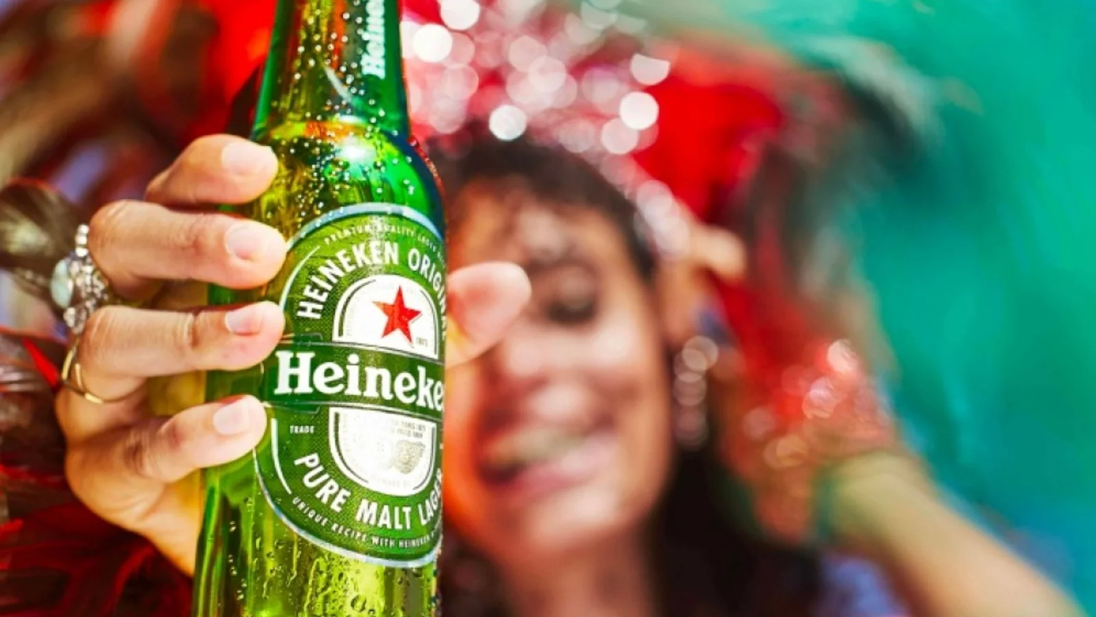 A hand holding a green Heineken bottle at a party