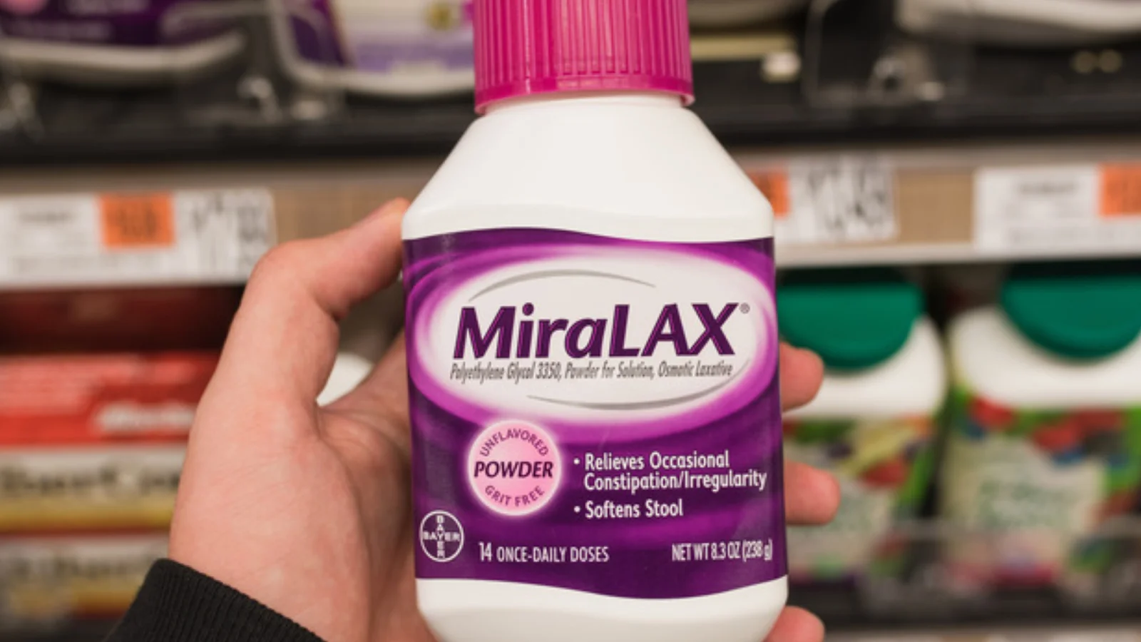 A hand holding a bottle of MiraLAX in a pharmacy aisle