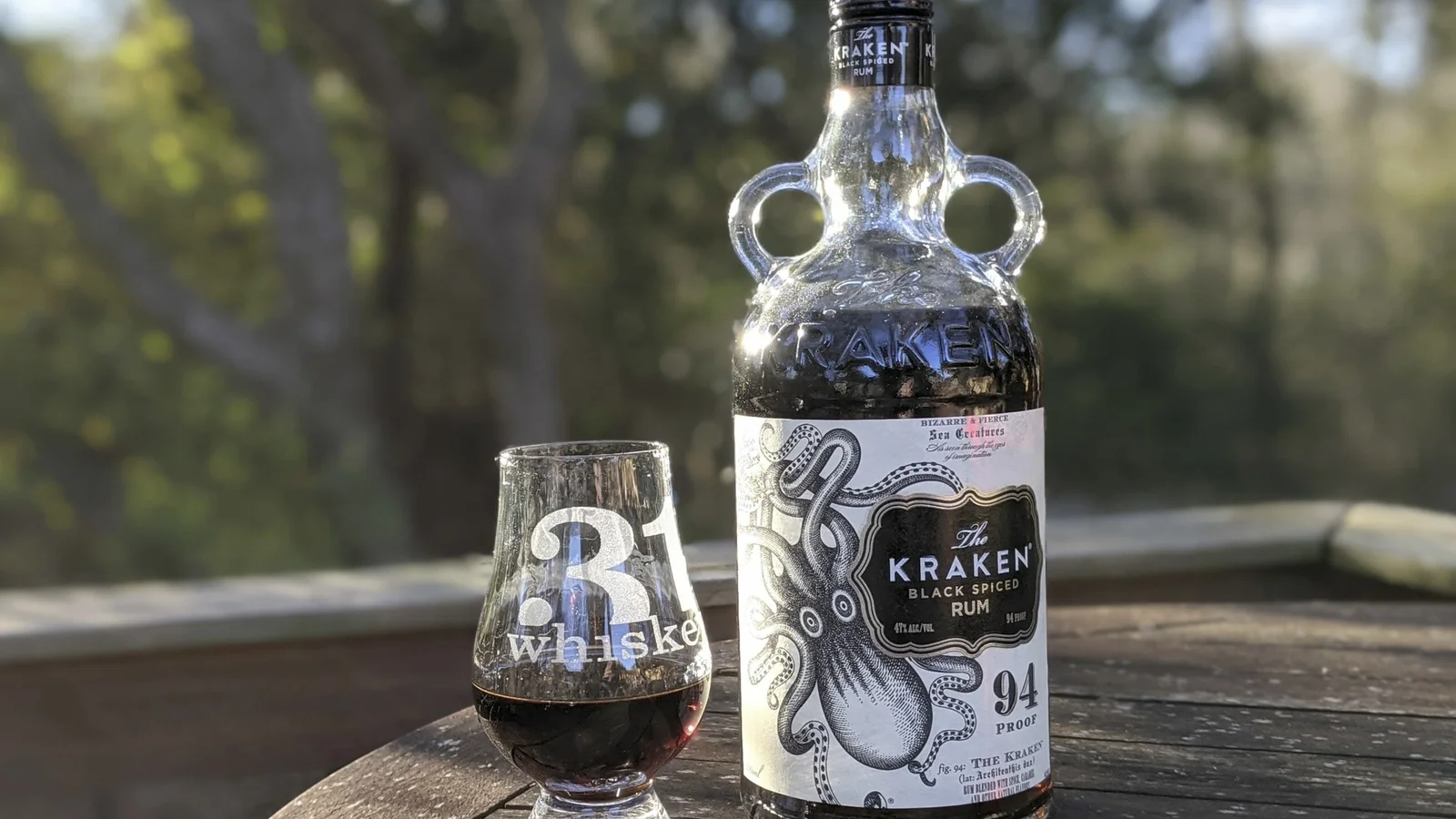 A bottle of The Kraken black spiced rum with a glass on a garden table