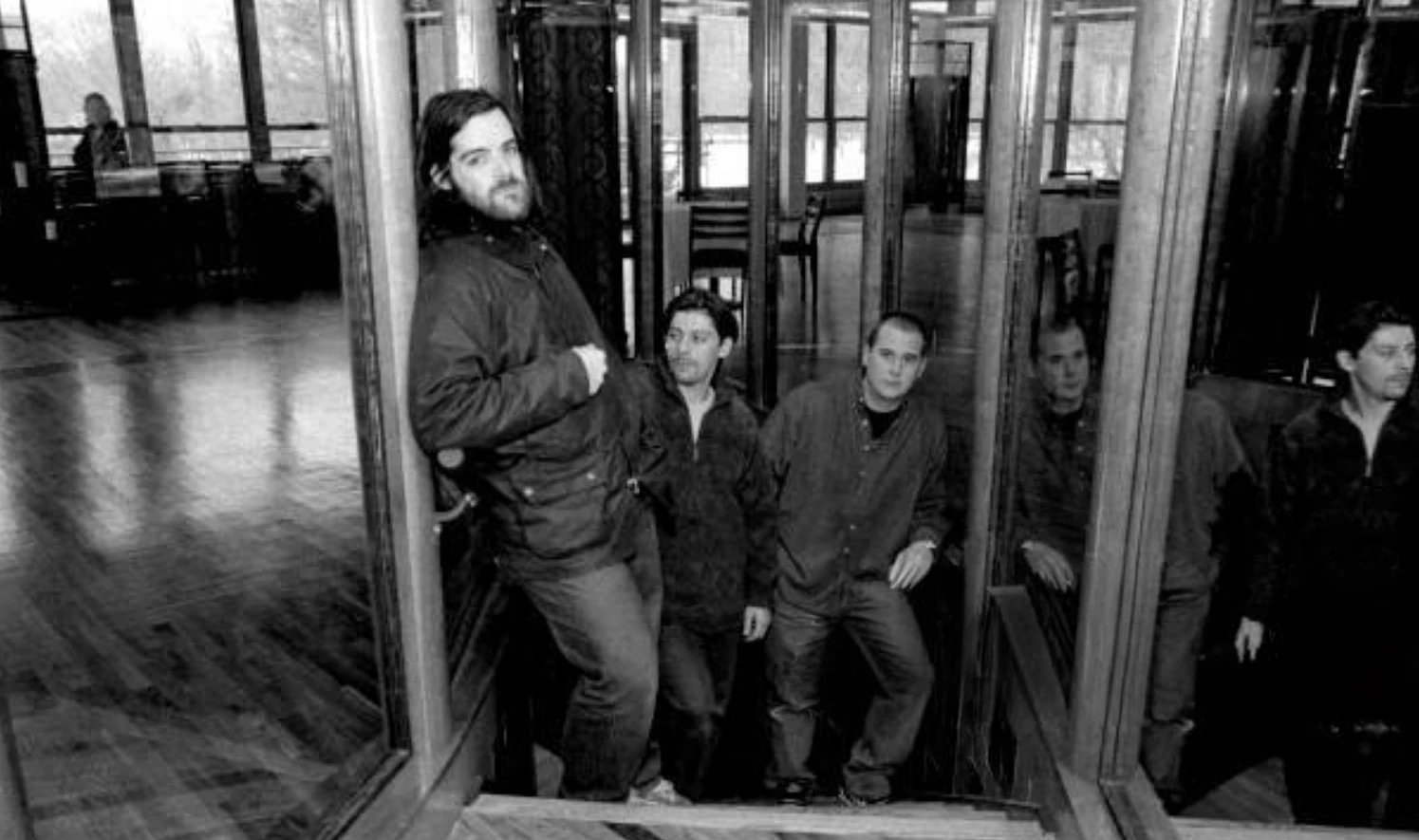 Black and white photo of the young Rockstar Games founding team standing on a wooden staircase, Sam Houser at the front