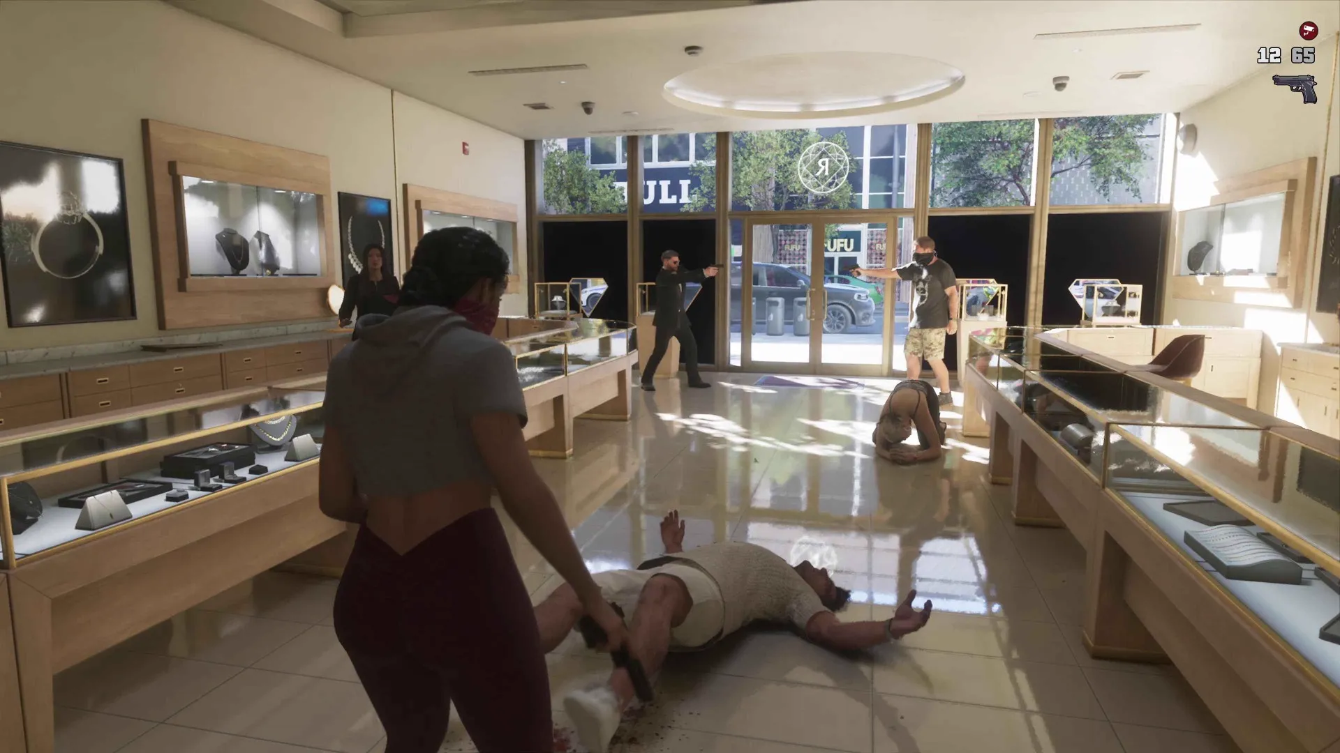 Lucia in a grey hoodie and red face bandana holds a pistol over a downed man between glass display cases in a GTA 6 jewellery store while masked accomplices cover the door and customers lie on the floor