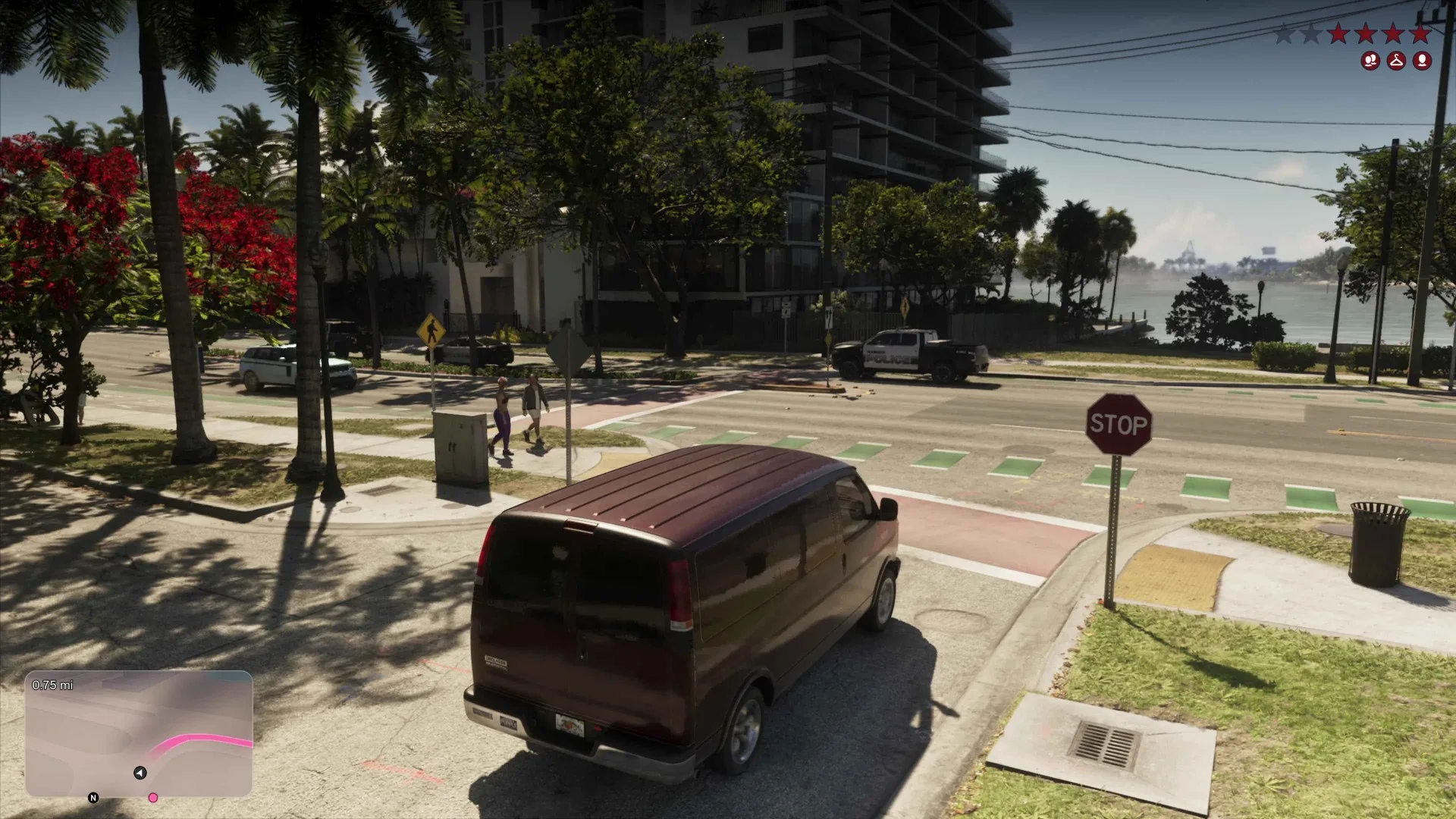 A maroon van waits at a stop sign near a police truck in GTA 6 while wanted stars and character icons show in the top right corner.