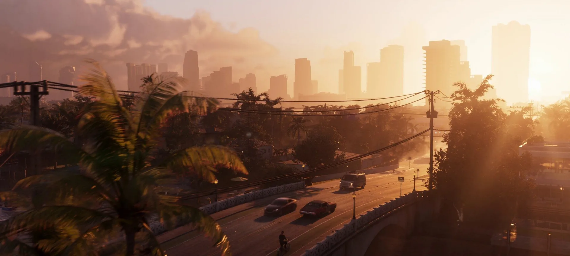 A hazy sunset skyline of downtown towers behind palm trees as cars and a cyclist cross a bridge in GTA 6