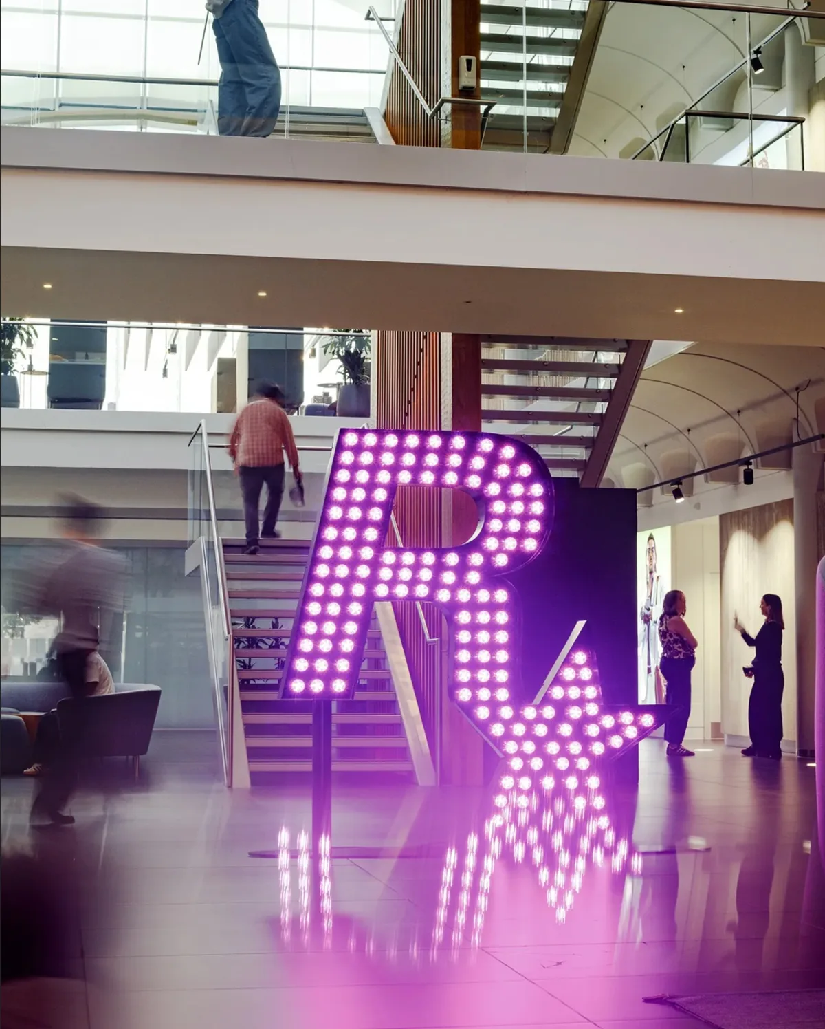 A glowing Rockstar logo in purple lights beside a staircase inside the Rockstar North studio