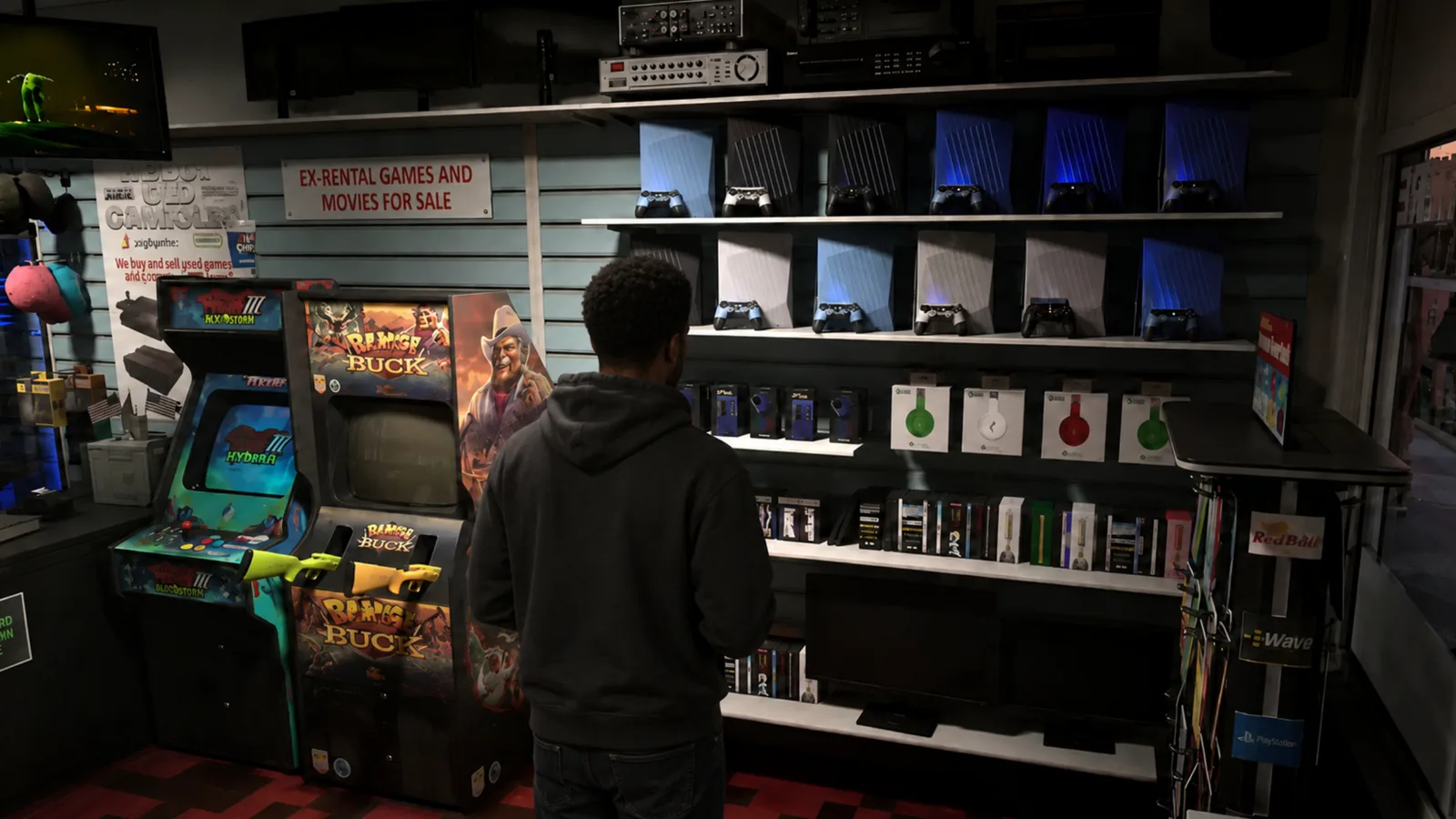 Customer in a hoodie browsing a wall of consoles, controllers and headphones beside arcade cabinets in a GTA 6 game store