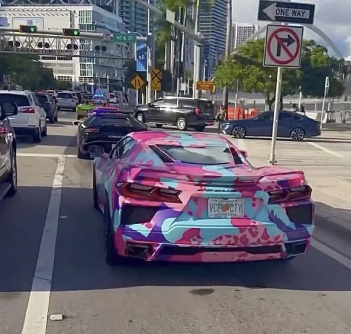 A Corvette wrapped in pink and blue camo with a VCE CTY Leonida plate waiting in Miami traffic