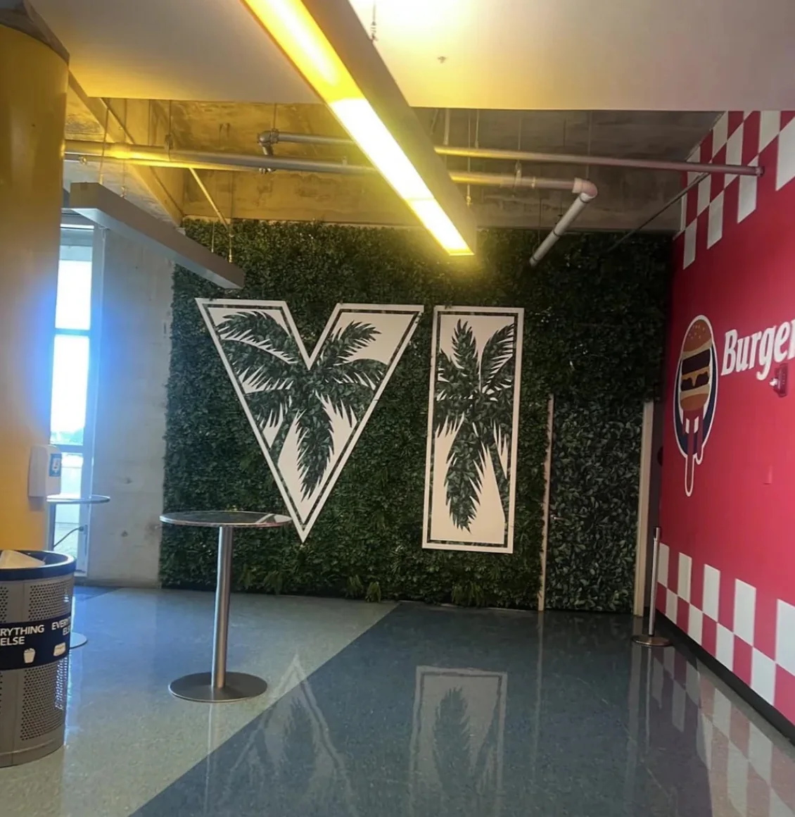 A VI logo made of palm-print panels on a hedge wall beside the Burger Shot stand at the Kaseya Center