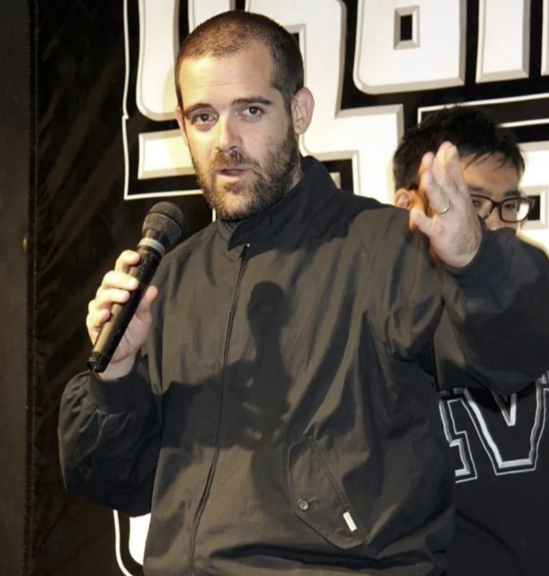 Sam Houser speaking into a microphone in front of a Grand Theft Auto logo backdrop