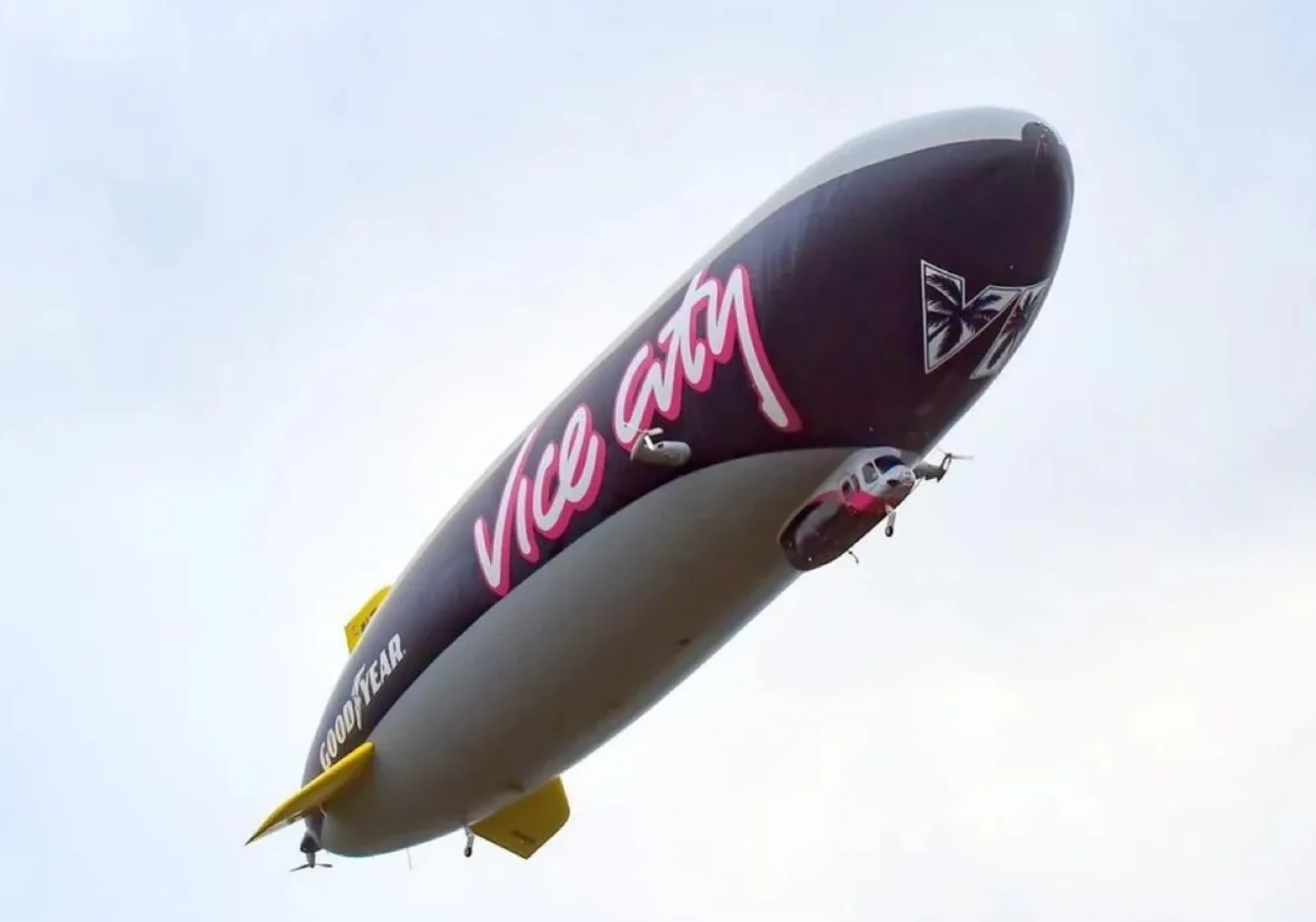 The Vice City zeppelin seen from below against a pale sky, showing the pink Vice City script, the VI palm logo and the Goodyear wordmark