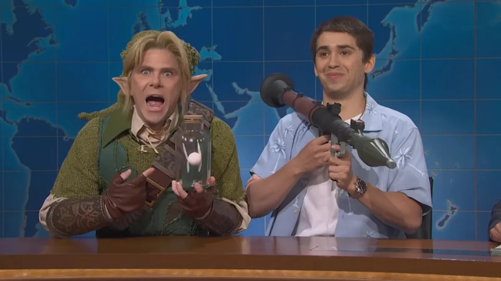 Mikey Day as Link holding a fairy in a bottle beside Marcello Hernández as Jason Duval with a rocket launcher at the Weekend Update desk