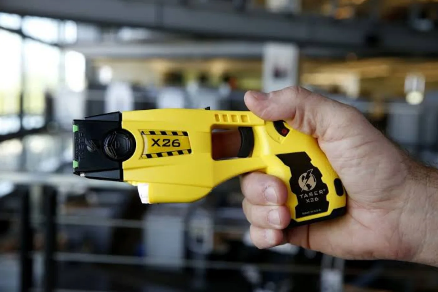 Hand holding a yellow and black Axon TASER X26, the real-world basis for the GTA 6 Coil Shocker.