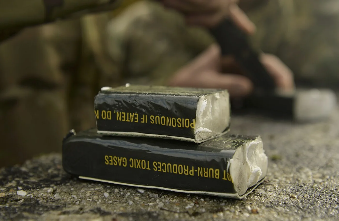 Two wrapped C-4 demolition blocks with warning print stacked on the ground, the real-world basis for the GTA 6 Sticky Bomb.